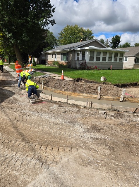 Crew setting curb forms next to a house, with fresh concrete poured along the street
