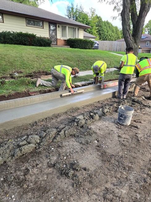 Four workers in safety vests smoothing a freshly poured concrete curb